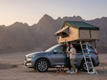 Load image into Gallery viewer, DesertX Nomad Plus rooftop tent in tan and dark green, with an extended space and ladder, mounted on a grey SUV.