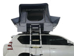 Load image into Gallery viewer, DesertX Basecamp hardshell rooftop tent on a white SUV, featuring a dark blue and grey fabric with a ladder.
