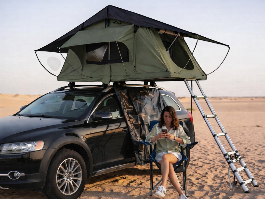 DesertX Nomad large rooftop tent in olive green on a black car, with a woman sitting in a chair nearby.