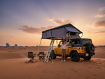 Load image into Gallery viewer, DesertX Nomad Plus rooftop tent on yellow Jeep in desert at sunset. Two people interacting with tent.