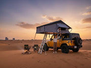 DesertX Nomad Plus rooftop tent on yellow Jeep in desert at sunset. Two people interacting with tent.
