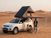 DesertX Trailblazer two-person hard shell rooftop tent mounted on a white SUV, with an attached awning.